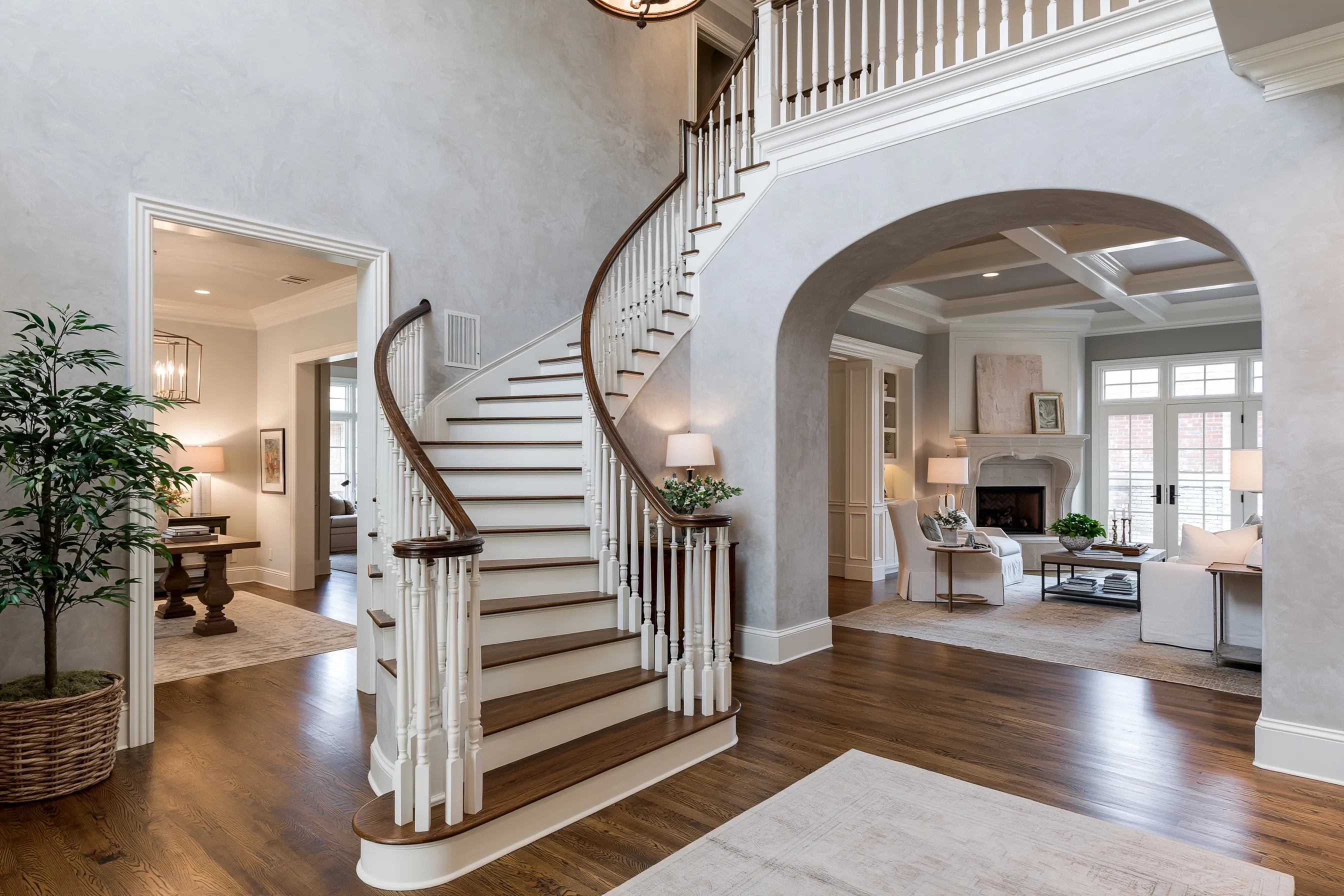 Two-story entry hall with a curved staircase, pale gray limewash walls and an arched opening to the living room